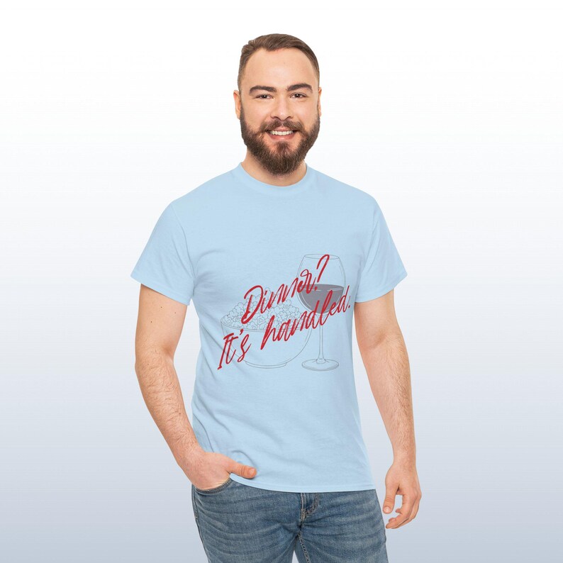 May include: Pale blue t-shirt featuring the red text "Dinner? It's handled." with a wine glass and plate graphic. The person is wearing blue jeans.