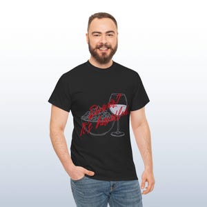 May include: Black t-shirt featuring a graphic of popcorn and a wine glass. Red script text reads "Show what I like, It's popcorn". A casual wear item.