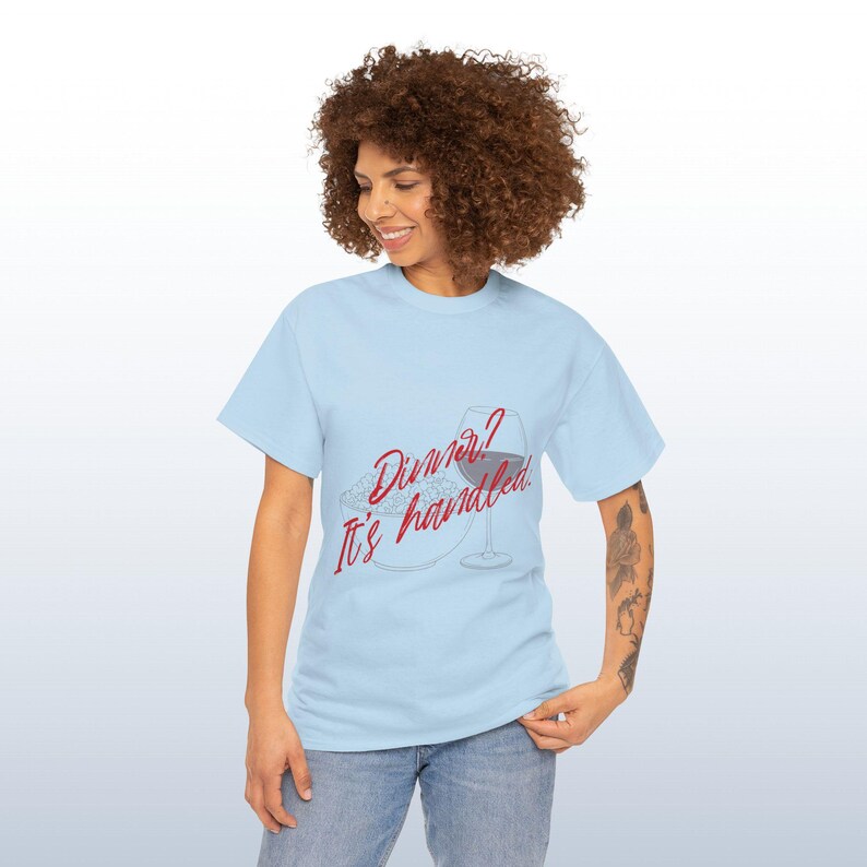 May include: Pale blue t-shirt featuring the red text "Dinner? It's handled". The design includes a plate of food and a wine glass. The shirt is made of a soft material.