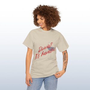 May include: Beige t-shirt featuring the text "Dinner? It's handled" in red script. The design includes a plate of food and a wine glass with red wine. The shirt is worn by a person.