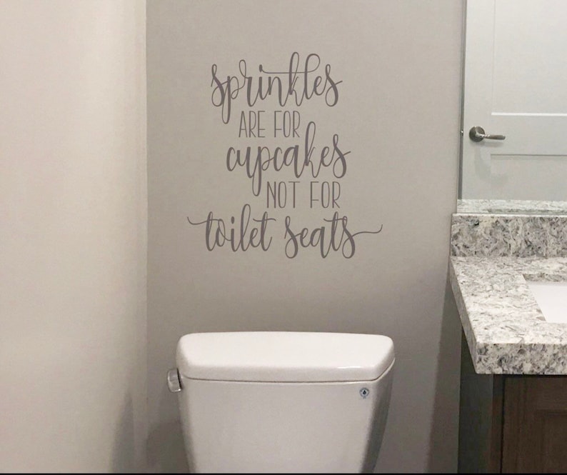 May include: A white toilet with a gray wall decal that reads "Sprinkles are for cupcakes not for toilet seats".