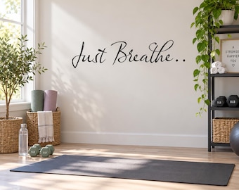 Puede incluir: Un adhesivo de pared de vinilo negro con el texto en cursiva Just Breathe y dos puntos al final. Las letras están aplicadas sobre una pared de color blanco roto, sirviendo como elemento decorativo en una habitación con esterilla, pesas y plantas.