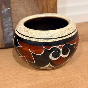 Vasija/olla de cerámica mexicana pintada a mano: arte popular rústico en tonos crema, negro y marrón rojizo.