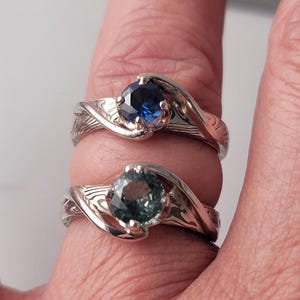 Shown is a set of engagement rings for same sex matching set.  The engagement ring set shows two unique handmade rings in gold with Montana Sapphire stones.