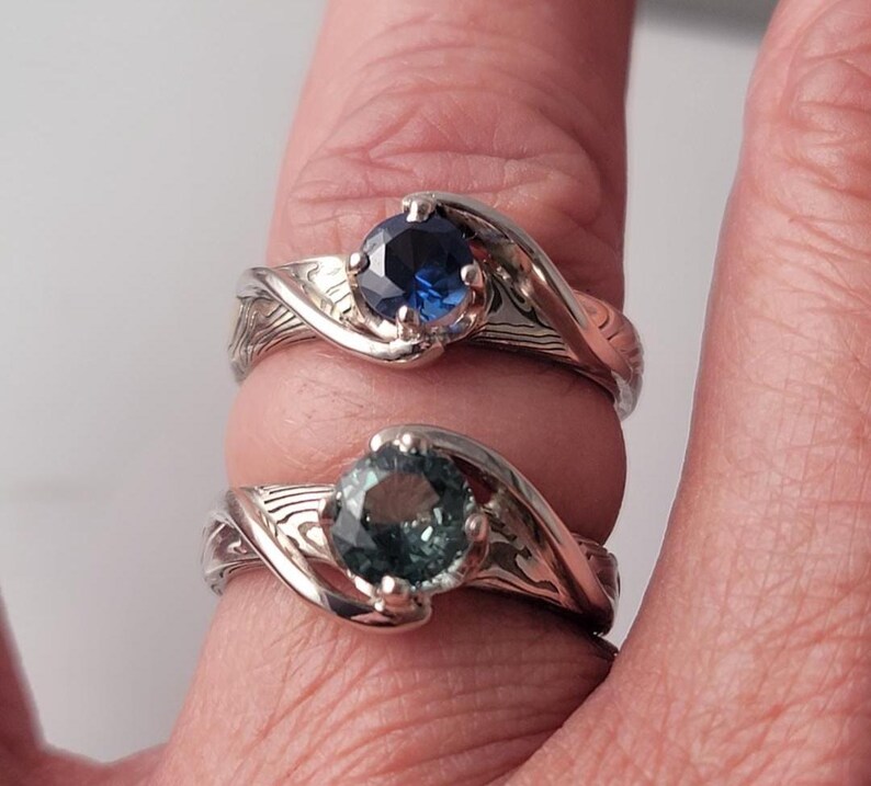 Shown is a set of engagement rings for same sex matching set.  The engagement ring set shows two unique handmade rings in gold with Montana Sapphire stones.