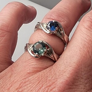 Shown is a set of engagement rings for same sex matching set.  The engagement ring set shows two unique handmade rings in gold with Montana Sapphire stones.