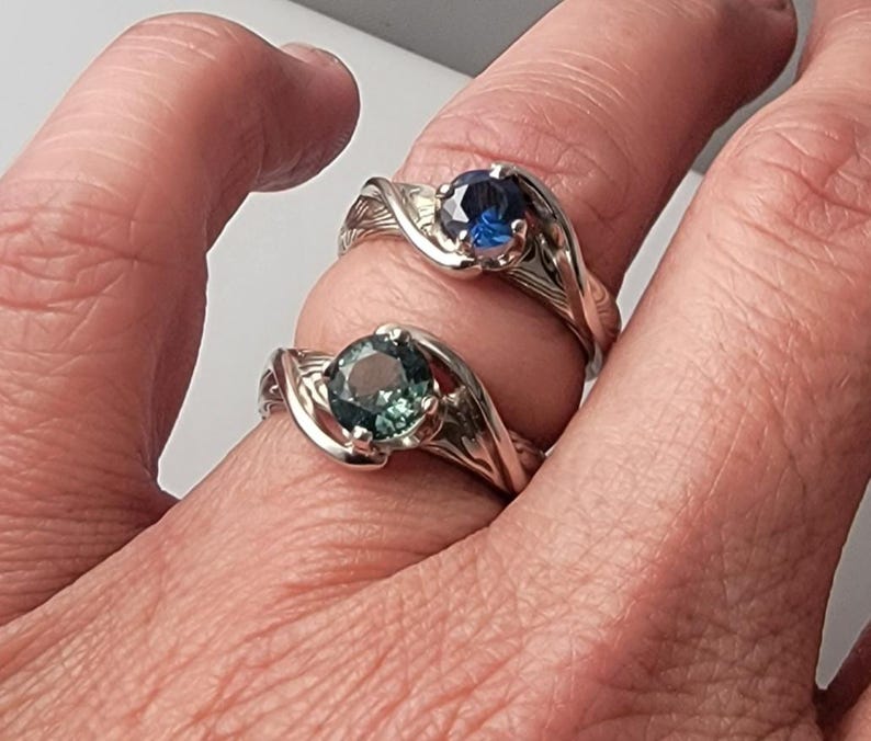 Shown is a set of engagement rings for same sex matching set.  The engagement ring set shows two unique handmade rings in gold with Montana Sapphire stones.