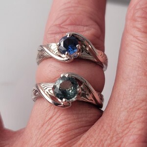 Shown is a set of engagement rings for same sex matching set.  The engagement ring set shows two unique handmade rings in gold with Montana Sapphire stones.