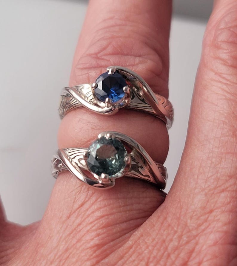 Shown is a set of engagement rings for same sex matching set.  The engagement ring set shows two unique handmade rings in gold with Montana Sapphire stones.