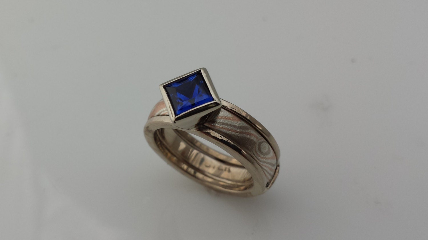 Mokume Gane Band with ring guard full bezel setting example shows square cut Blue Sapphire