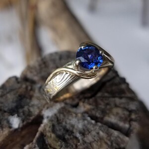 Bright Blue sapphire stone in a mokume gane ring.  The stone is held by gold waves.  Unique mokume gane  engagement ring