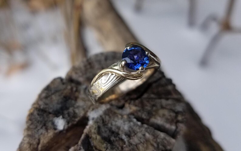 Bright Blue sapphire stone in a mokume gane ring.  The stone is held by gold waves.  Unique mokume gane  engagement ring