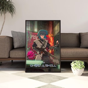 Puede incluir: Un póster enmarcado que muestra a un personaje de anime con cabello azul, vistiendo un abrigo claro y sosteniendo un arma de fuego larga. El fondo muestra un vehículo rojo y elementos industriales. El texto "THE GHOST IN THE SHELL" aparece abajo.