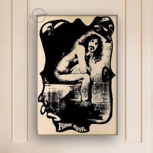 Puede incluir: Lámina artística enmarcada en blanco y negro con una ilustración estilizada de Frank Zappa. La obra representa una figura sentada en un inodoro, con el texto "FRANK ZAPPA" en la parte inferior. La impresión está montada en un marco blanco.