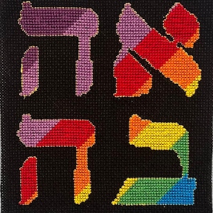 May include: A square black cross-stitch fabric piece featuring four Hebrew letters embroidered in a vibrant, multi-colored gradient pattern. The letters are arranged in a two-by-two grid, showcasing shades of purple, red, orange, yellow, green, and blue.