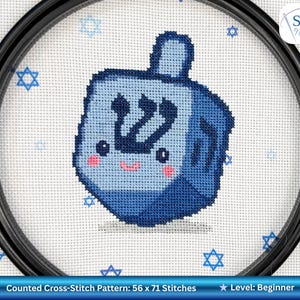 May include: A counted cross-stitch pattern featuring a blue dreidel with a smiling face and Hebrew letters. The pattern is surrounded by Star of David symbols and is 56 x 71 stitches. The level is beginner.