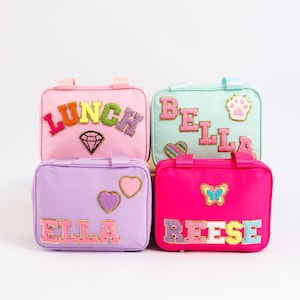 May include: Four colorful lunch bags in pink, mint green, purple, and hot pink. Each bag has a name or word spelled out in colorful, textured letters. Embellishments include a diamond, paw print, hearts, and a butterfly.
