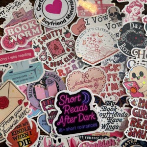 May include: A collection of colorful stickers with various designs and text. The stickers feature book-related themes, including the words "Book Worm," "Smutty," and "Book Club." Other stickers have phrases like "Short Reads After Dark" and "I Vow." The stickers are in various shapes and sizes.