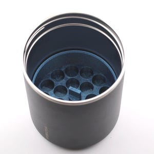 Puede incluir: Un vaso negro con borde plateado e interior azul. El interior presenta un inserto azul con m&uacute;ltiples hendiduras circulares. El vaso est&aacute; dise&ntilde;ado para contener objetos peque&ntilde;os.