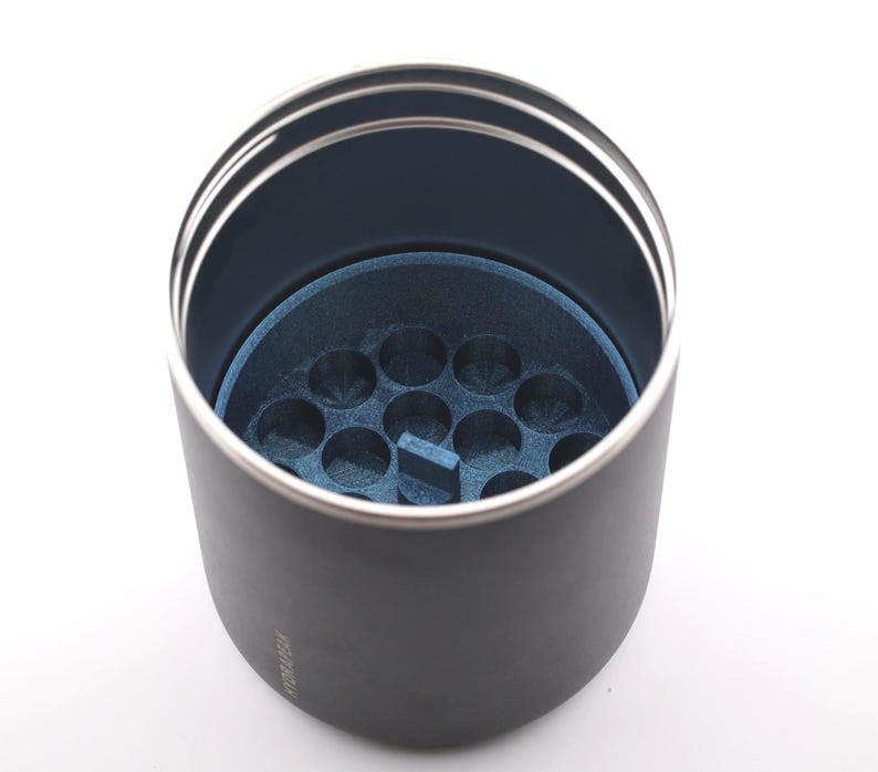 Puede incluir: Un vaso negro con borde plateado e interior azul. El interior presenta un inserto azul con m&uacute;ltiples hendiduras circulares. El vaso est&aacute; dise&ntilde;ado para contener objetos peque&ntilde;os.