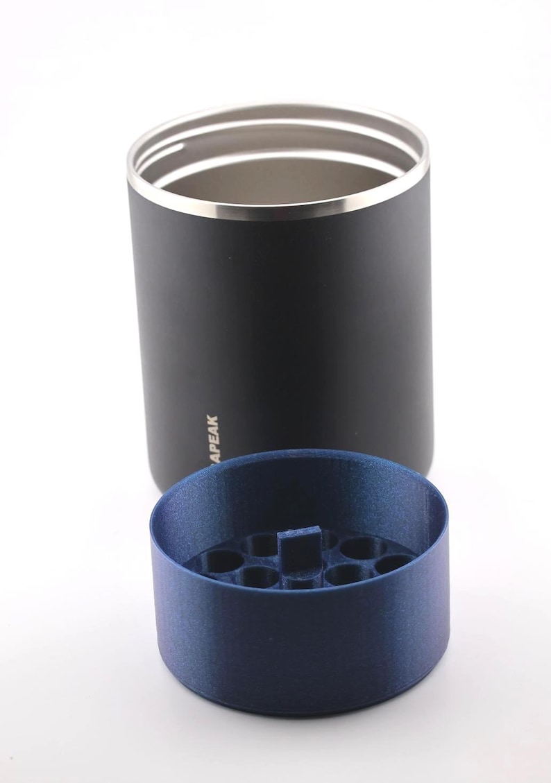 Puede incluir: Un vaso negro con borde plateado y la palabra "APEAK" impresa en el lateral. Un inserto azul cil&iacute;ndrico con m&uacute;ltiples agujeros se encuentra delante del vaso. El vaso est&aacute; probablemente dise&ntilde;ado para contener bebidas.