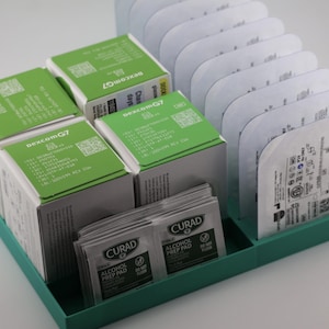 May include: A teal tray contains boxes with green tops marked "dexcom G7", individual sealed packets, and alcohol prep pads. The boxes are white with green text and graphics.