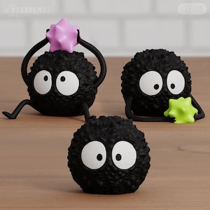 Peut inclure: Trois figurines de suie noires avec de grands yeux blancs et des pupilles noires. Une figurine tient une étoile rose au-dessus de sa tête, une autre tient une étoile vert citron, et la troisième est une forme ronde simple. Surfaces texturées.