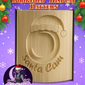 Könnte beinhalten: Ein Buchfalt-Display-Muster mit einem Santa Cam-Design. Das beige Buch hat einen Weihnachtsmannhut und die Worte "Santa Cam" sind in die Seiten geschnitzt. Das Bild hat Weihnachtsdekorationen im Hintergrund, darunter Ornamente und Girlanden.