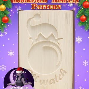 Könnte beinhalten: Ein Buchfalt-Display-Muster mit Weihnachtsthema. Das Buch ist mit einem Weihnachtsmützen-Design und dem Wort "watch" geschnitzt. Der Hintergrund ist lila mit Weihnachtsschmuck und Schneeflocken. Das Logo von Moonlit Munchkin Creations befindet sich unten links.