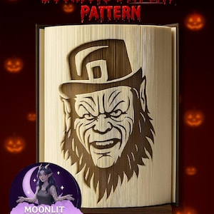 Może przedstawiać: Wzór wyświetlania książki z wyrzeźbionym wizerunkiem twarzy leprechauna. Tekst "Bookfold DISPLAY PATTERN" znajduje się na górze. Obraz jest umieszczony na ciemnoczerwonym tle z dyniami. Logo Moonlit Munchkin Creations znajduje się na dole.