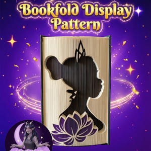 May include: A bookfold display pattern with a silhouette of a woman's profile and a lotus flower cut into the pages. The text "Bookfold Display Pattern" is in gold lettering. The background is purple with stars and confetti.