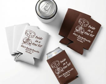 Puede incluir: Imagen superior de enfriadores de latas blancos y marrones con el texto "bride in a tini bit" y "Mia's Bachelorette AUSTIN, TX EST.2026". Se ve una lata plateada. Foto de producto.