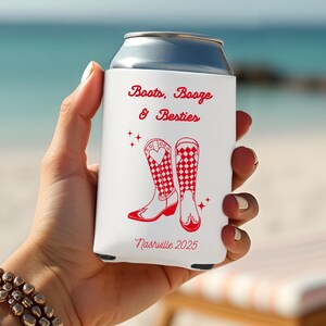K&ouml;nnte beinhalten: Ein wei&szlig;er Getr&auml;nkedosenk&uuml;hler mit rotem Text und Grafiken. Der Text lautet "Boots, Booze & Besties" und "Nashville 2025". Die Grafik zeigt zwei rote Cowboy-Stiefel mit Herz- und Karomustern.