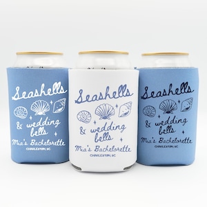 May include: Three can coolers in light blue and white, each featuring the text "Seashells & wedding bells" with seashell illustrations. The text "Mia's Bachelorette, Charleston SC" is also printed on the coolers.
