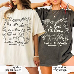 Könnte beinhalten: Übergroße T-Shirts in Elfenbein und Pfeffer mit einem weißen Grafikdesign. Das Design enthält den Text "a Bride in a 'tini bit tipsy" und "Amelia's Bachelorette, Scottsdale, AZ" mit Illustrationen von Cocktails, Schleifen und Herzen.