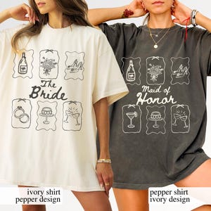 May include: Two oversized t-shirts, one ivory and one pepper-coloured, with wedding-themed graphics. The ivory shirt reads "The Bride", the pepper shirt says "Maid of Honor". Each shirt has six illustrated icons.
