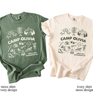 May include: Two short-sleeve crew neck t-shirts, one moss green with an ivory graphic and one ivory with a moss green graphic. Both feature the text CAMP OLIVIA, AUGUST 2026, BRECKENRIDGE, CO, and illustrations of mountains, a canoe, a tent, and camping gear.