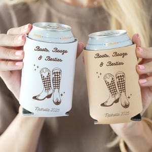 K&ouml;nnte beinhalten: Zwei Getr&auml;nke-K&uuml;hlmanschetten, eine wei&szlig;e und eine beige, mit dem Text "Boots, Booze & Besties" und "Nashville 2025". Jede hat eine braune Illustration von Cowboy-Stiefeln. Zum K&uuml;hlen von Getr&auml;nken.