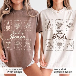 May include: Two t-shirts, one in espresso and one in ivory, display wedding-related designs. The espresso shirt reads "Maid of Honor", while the ivory shirt says "The Bride". Both shirts have matching illustrations of a champagne bottle, bouquet, shoes, and other items.