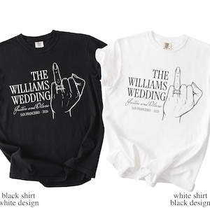 Op de afbeelding: Twee t-shirts, één zwart en één wit, elk met een afbeelding van een hand met de middelvinger omhoog, met een ring. De tekst luidt "THE WILLIAMS WEDDING Justin and Olivia SAN FRANCISCO - 2026".