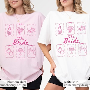 May include: Two oversized t-shirts, one pink and one white, each with a pink graphic. The design includes illustrations of a champagne bottle, bouquet, heels, rings, cake, and champagne glasses, with the text "The Bride".