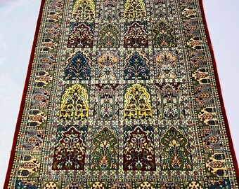 May include: Rectangular rug with a detailed floral pattern in red, blue, green, and yellow. The rug has a dark red border and a cream fringe. The design features repeating arch-shaped motifs. The rug is suitable for a living room.
