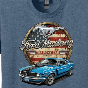 May include: Blue t-shirt featuring a graphic of a blue Ford Mustang car. The design includes the words "Ford Mustang" and "The Pony Car Since 1964" with a horse emblem and an American flag background.