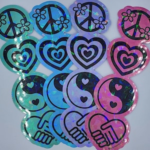 May include: A collection of holographic stickers in various shapes, including peace signs with flowers, layered hearts, yin-yang symbols, and clasped hands. The stickers have a rainbow sheen and are in shades of teal, blue, and pink.