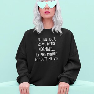 Peut inclure: Sweat-shirt noir avec l'inscription blanche "J'AI, UN JOUR, ESSAYÉ D'ÊTRE NORMALE... LA PIRE MINUTE DE TOUTE MA VIE". La personne porte des lunettes de soleil en forme de cœur et a les cheveux argentés.