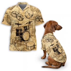 May include: A beige button-down shirt and a dog shirt, both featuring a vintage-style drum set design with musical notes. The shirts have short sleeves and a collared neckline. The dog is a dachshund.