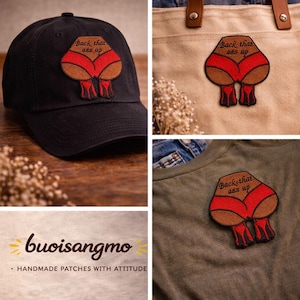Può includere: Cappellino da baseball nero con una toppa raffigurante un disegno a cartoni animati di una vista posteriore con biancheria intima rossa e tacchi alti. Il testo "Back that ass up" è sopra il disegno. L'immagine mostra anche la toppa su una borsa tote e una maglietta.