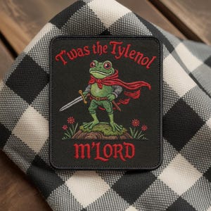 Può includere: Toppa ricamata con una rana verde con mantello rosso e spada. La toppa recita "T'was the Tylenol m'Lord" in testo rosso. La toppa è quadrata con bordo nero e si trova su uno sfondo a scacchi bianco e nero.