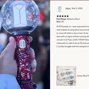 May include: Two bedazzled light sticks, one in shades of blue and silver, the other in red and pink, are held up. Each has a clear, spherical top with a white geometric design. The handles are covered in sparkling gems. The image is taken at a concert.