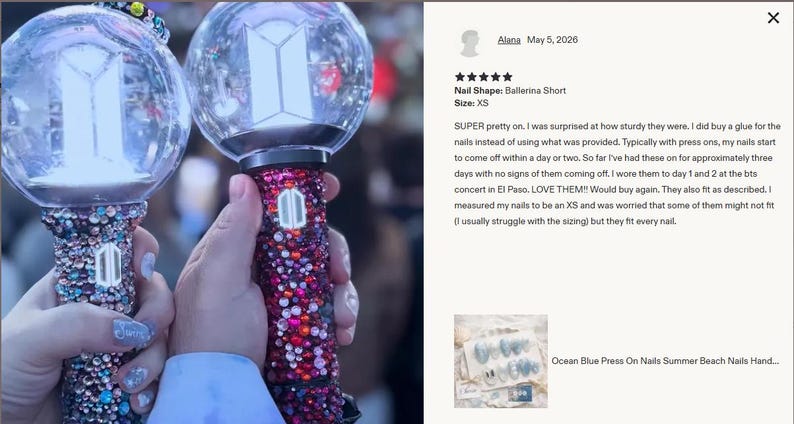 May include: Two bedazzled light sticks, one in shades of blue and silver, the other in red and pink, are held up. Each has a clear, spherical top with a white geometric design. The handles are covered in sparkling gems. The image is taken at a concert.